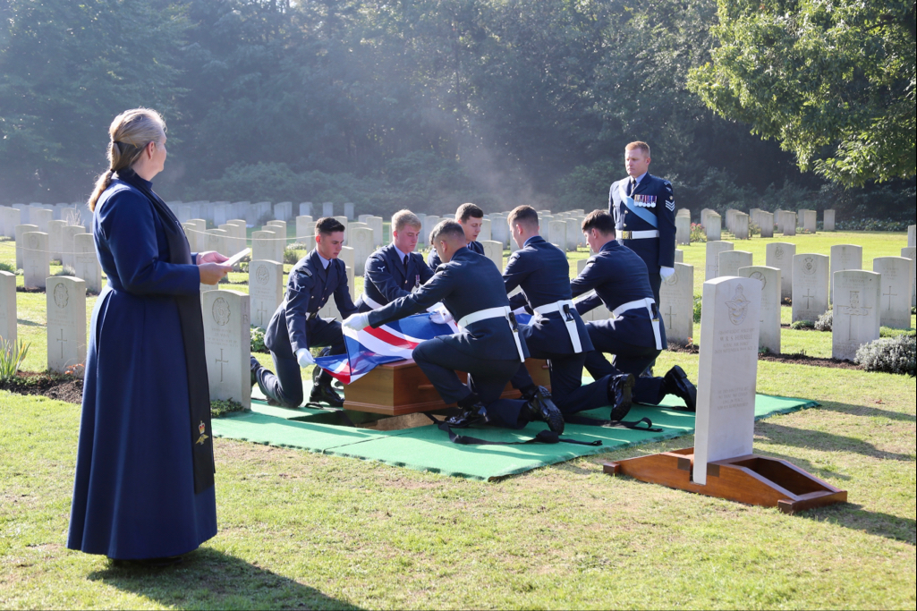 Image of Reverend in cemetery, while RAF aviators lay to rest the coffin.
